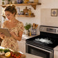 femme lit sa recette tout en gardant sa cuisinière protégée avec une  Protection plaque à induction